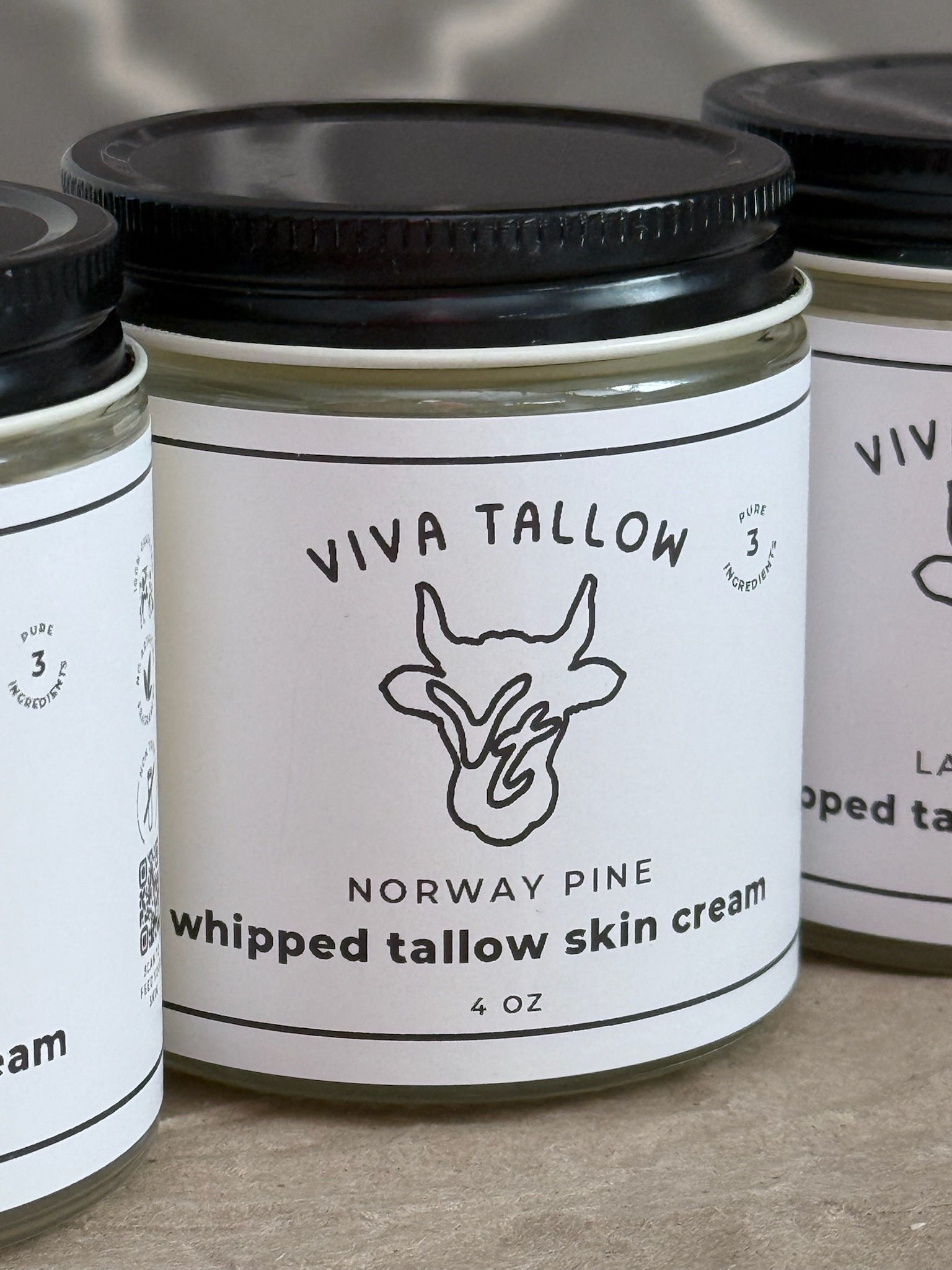 Jars of Viva Tallow Norway Pine whipped tallow skin cream on a neutral background